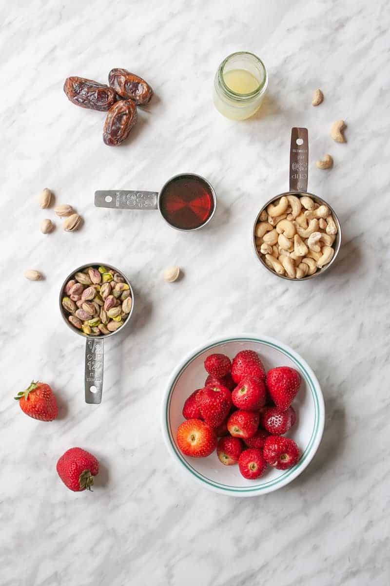 Ingredients for the dairy-free strawberry cheesecake. Dates, lemon juice, maple syrup, cashews, pistachios and strawberries.